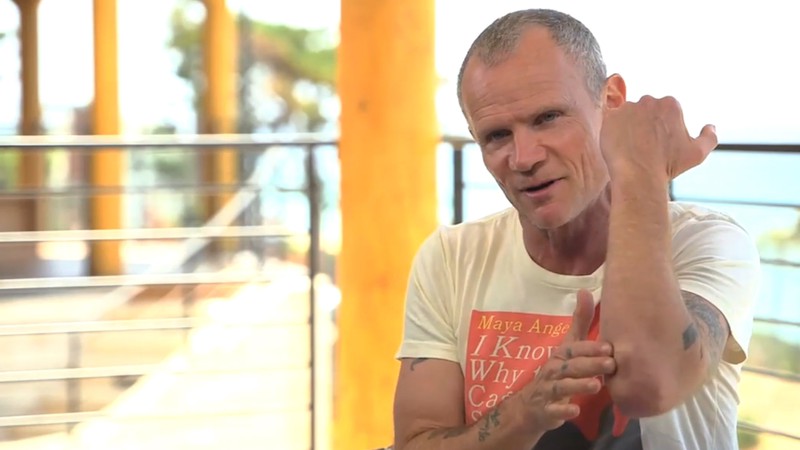 Flea, baixista do Red Hot Chili Peppers, mostrando a lesão no braso causada por um acidente enquanto ele praticava snowboarding - Reprodução/Vídeo