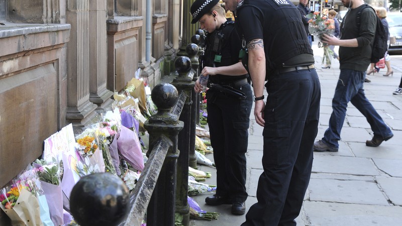 Policiais observam os tributos às vítimas do show do ataque terrorista ocorrido no show da cantora Ariana Grande em Manchester, na Inglaterra, em 23 de maio de 2017. As homenagens foram colocadas na praça St. Ann. 
 - AP