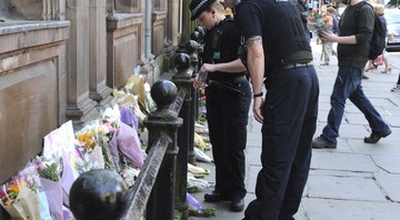 Policiais observam os tributos às vítimas do show do ataque terrorista ocorrido no show da cantora Ariana Grande em Manchester, na Inglaterra, em 23 de maio de 2017. As homenagens foram colocadas na praça St. Ann. 
 - AP