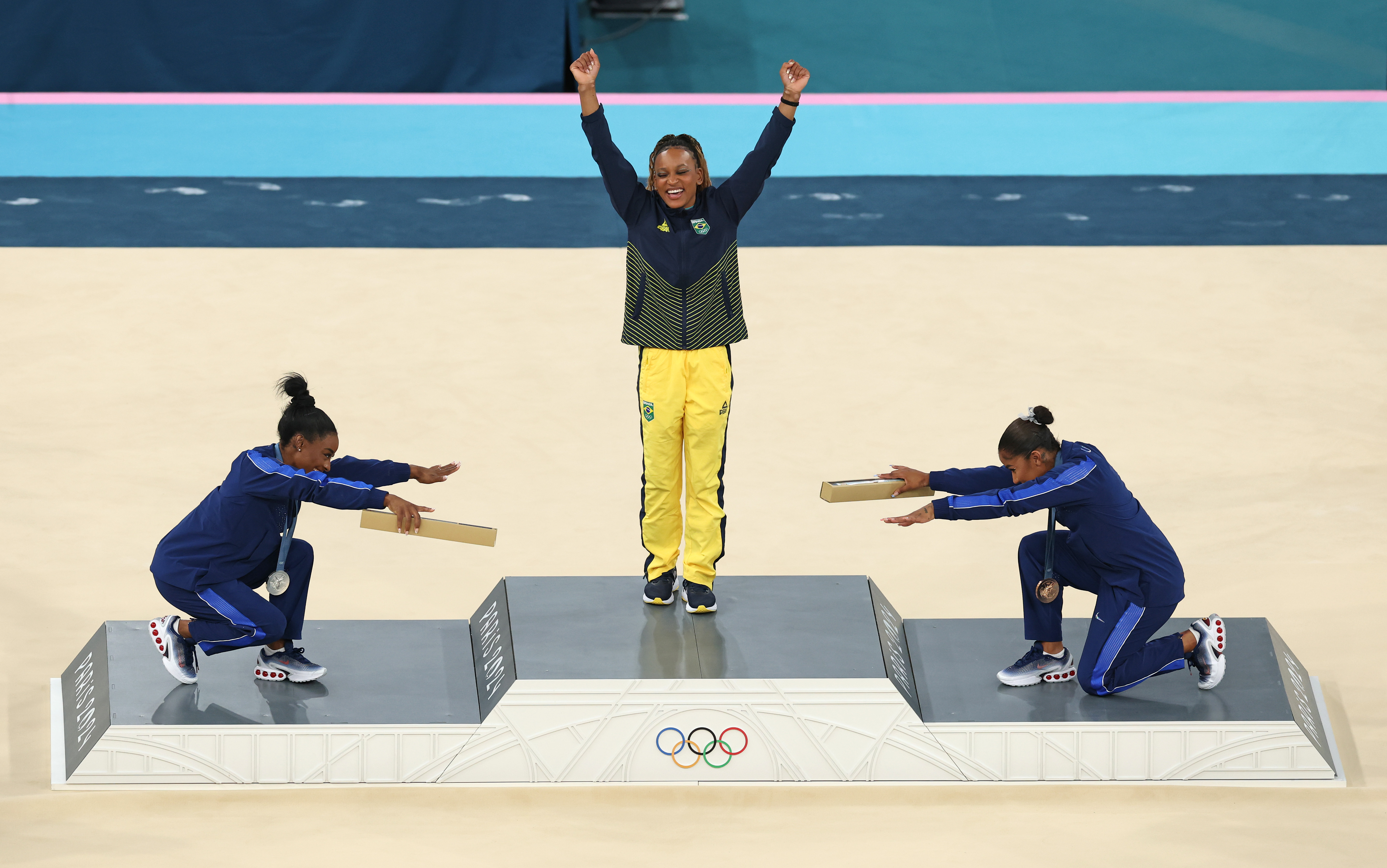 Rebeca Andrade no pódio, sendo saudada por Simone Biles e por Jordan Chiles (Foto: Elsa/Getty Images))