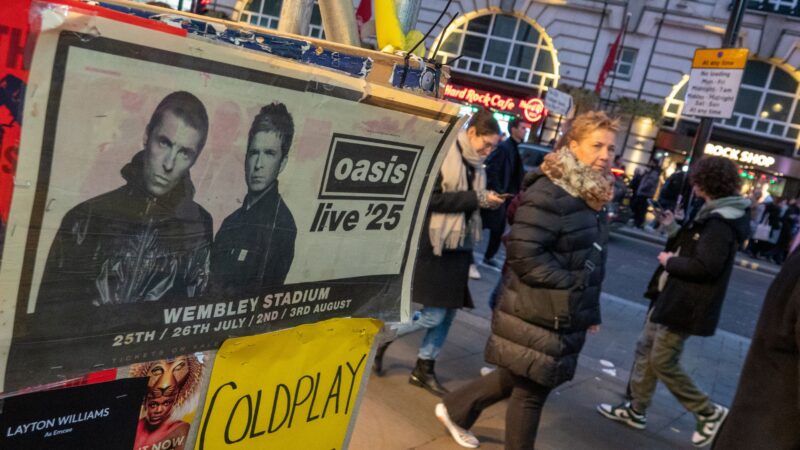 Pessoas na cidade de Londres passando próximo a um cartaz de show do Oasis (Foto: Matt Cardy/Getty Images)