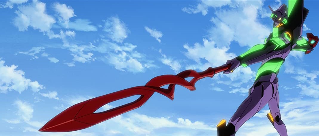 Audiodescrição resumida: É dia. Céu azul com poucas nuvens. Eva 01 segura uma lança vermelha e está com os braços flexionados.