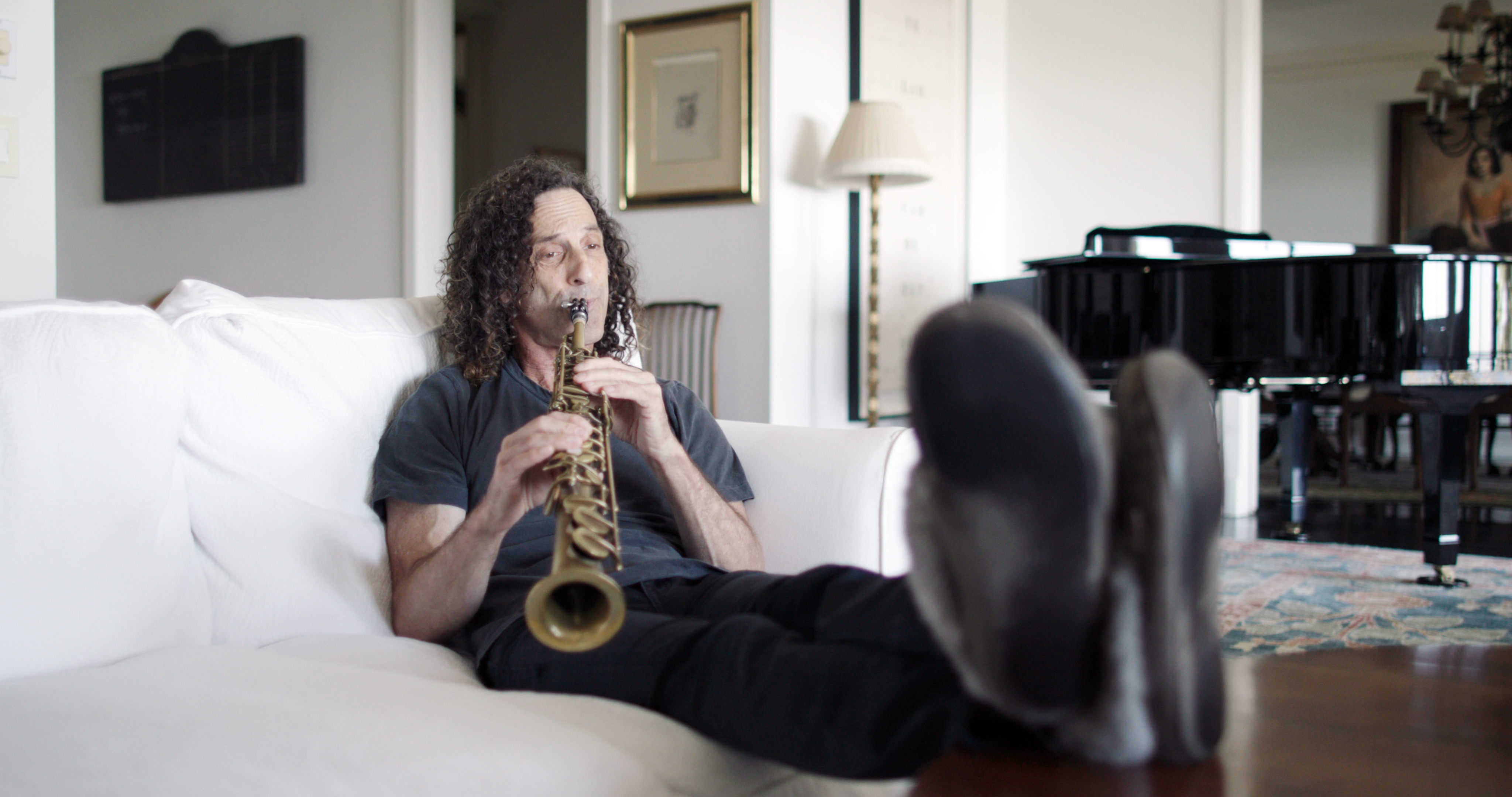 Kenny G toca sax sentado no sofá