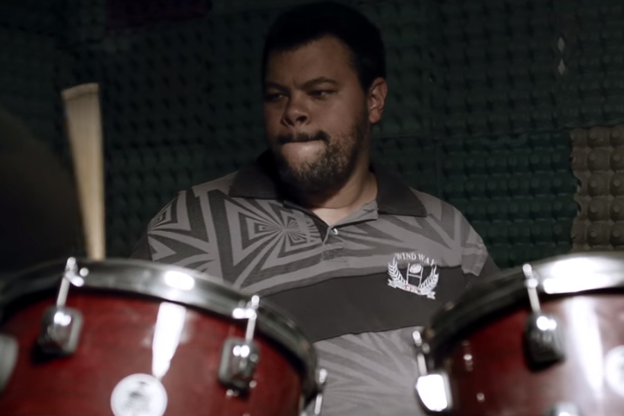 O ator Babu Santana dando vida ao personagem Santana enquanto ele toca bateria em cena do filme Mundo Cão, do diretor Marcos Jorge