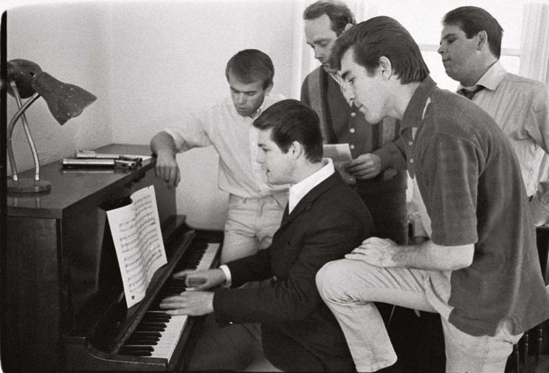 Em foto de 1964, Brian Wilson (ao piano) mostra uma nova composição para a banda. Junto a ele estão (da esq. para a dir.) Al Jardine, Mike Love, Dennis Wilson e Carl Wilson.