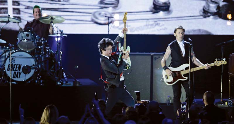 O Green Day em 2015, na apresentação do Hall da Fama do Rock; a capa de Revolution Radio, novo disco do trio