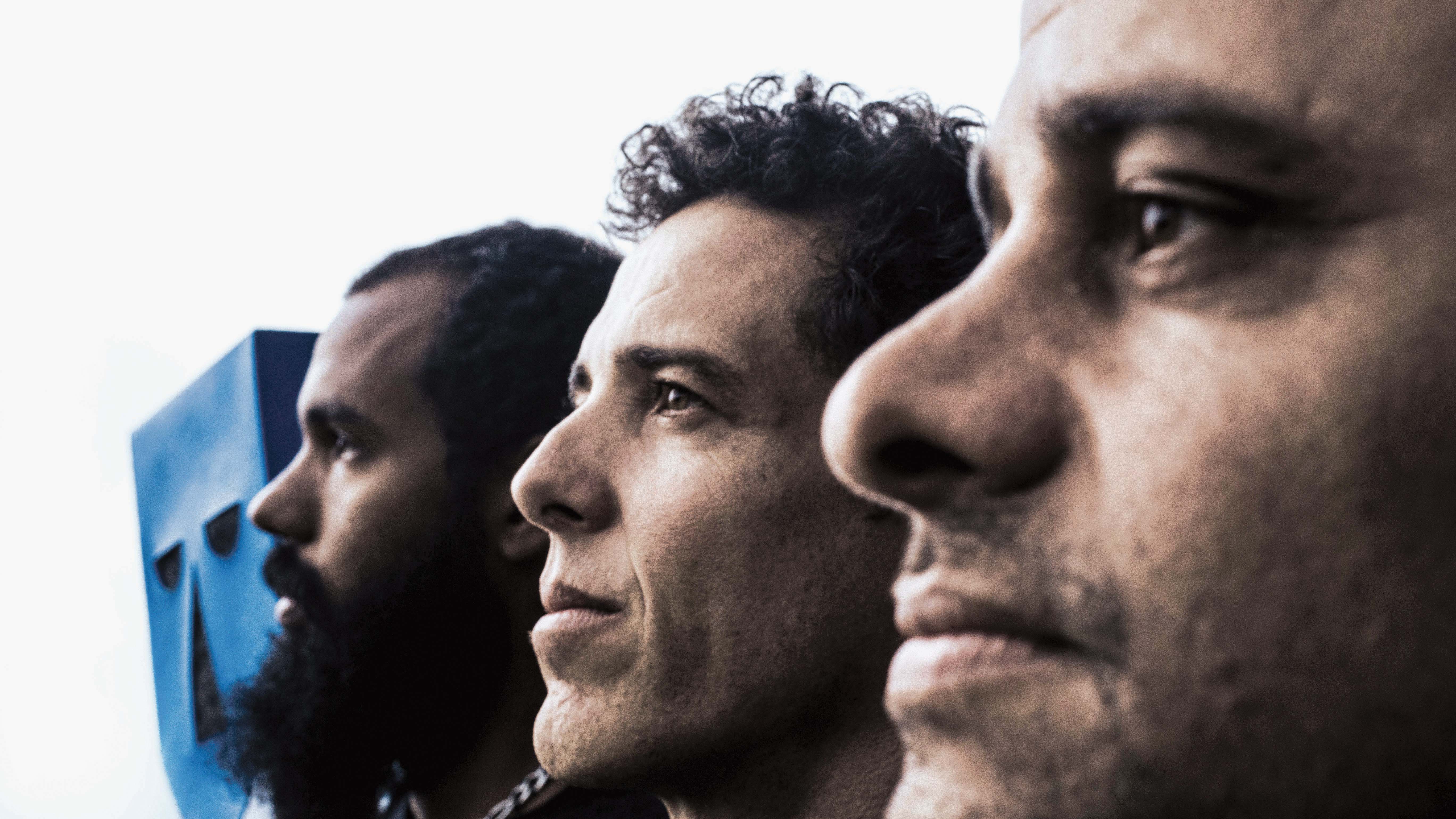 A parte sonora do BaianaSystem: (da esq. p/ a dir.) Russo Passapusso, SekoBass e Roberto Barreto. À esquerda, a máscara que é símbolo da banda, criada por Filipe Cartaxo